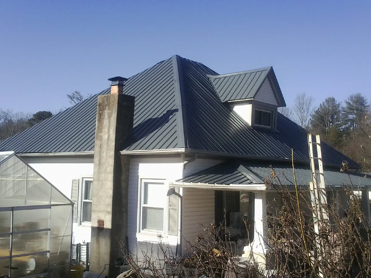 Dark blue standing seam metal roof on a white farmhouse with dormer — Slate & Tile Roof Repair by Roofing Brothers in Altavista