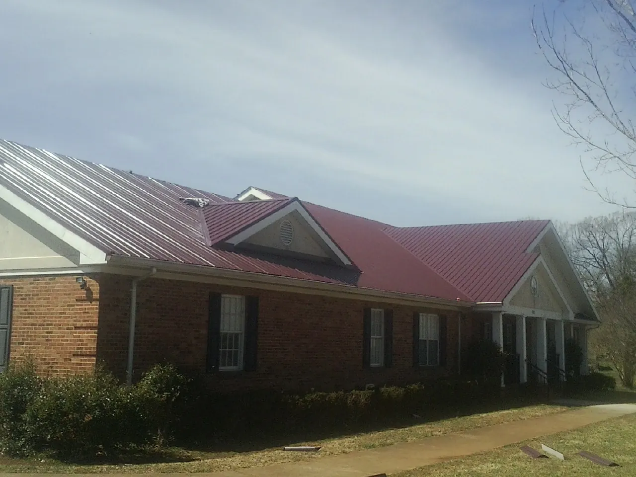 Red metal roof with gabled entries on a long brick building, from a Hail Damage Roof Repair job in Altavista