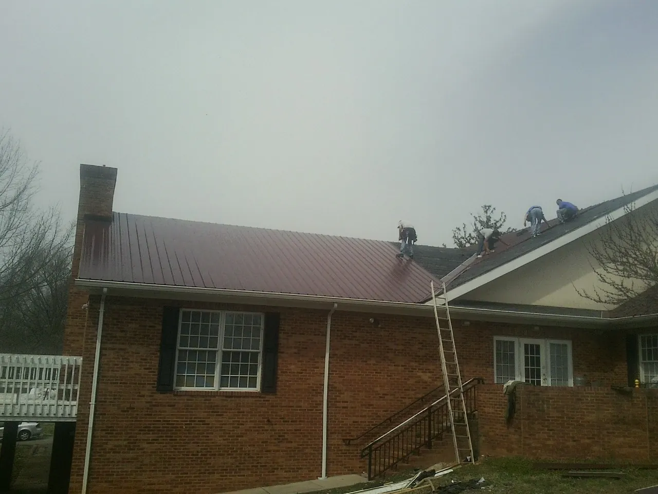 Crew setting red metal roofing panels on a brick home in Altavista