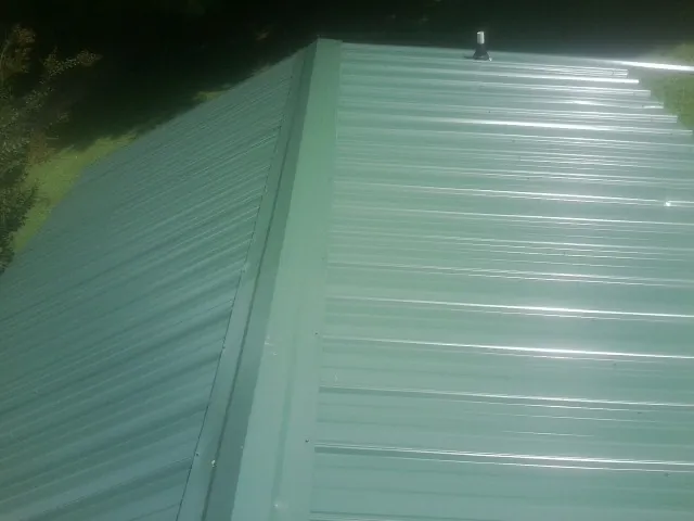 New green metal panels meeting at the ridge of a roof — Flat Roof Repair work by our crew in Altavista