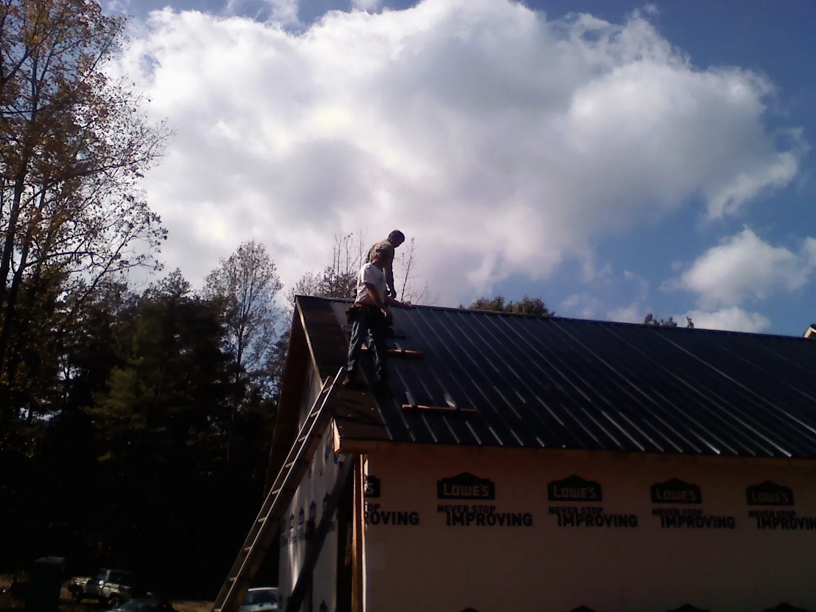 Roofer fastening dark metal panels high against a cloudy sky, from a Roof Inspection job in Altavista