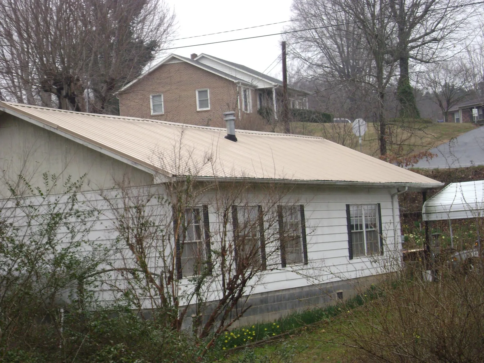 Tan metal roof on a white sided house set into a hillside — Commercial Roofing by Roofing Brothers in Altavista